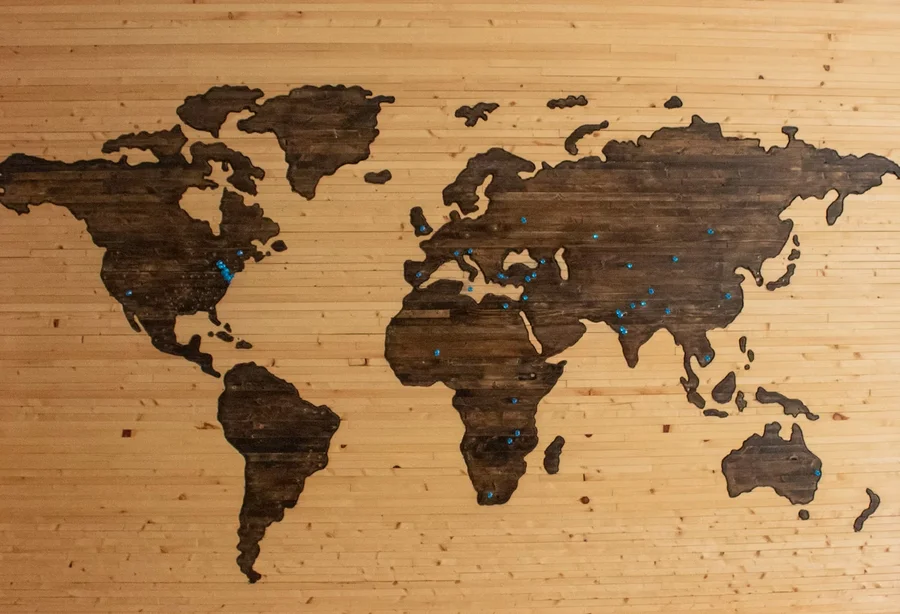 Wooden world map mounted on a wall with blue location pins marking sites across multiple countries